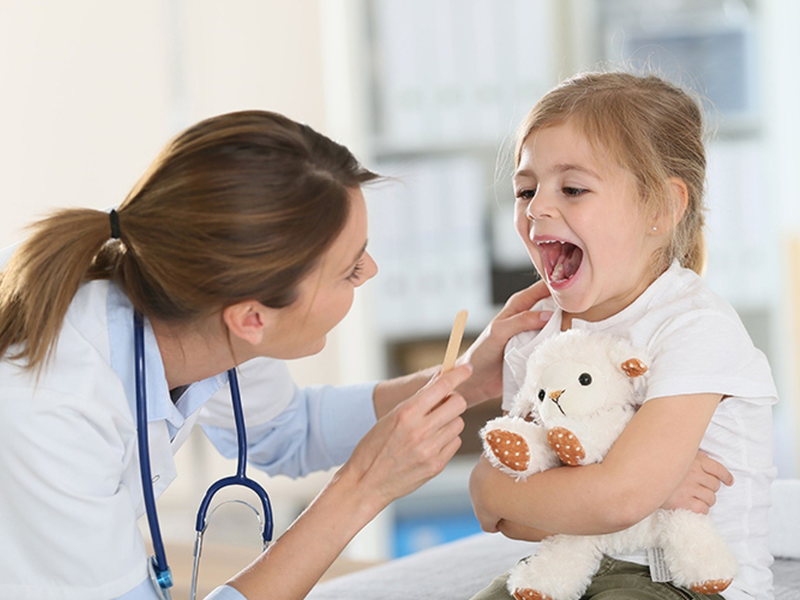 Médica examinando la garganta de una niña con bajalenguas