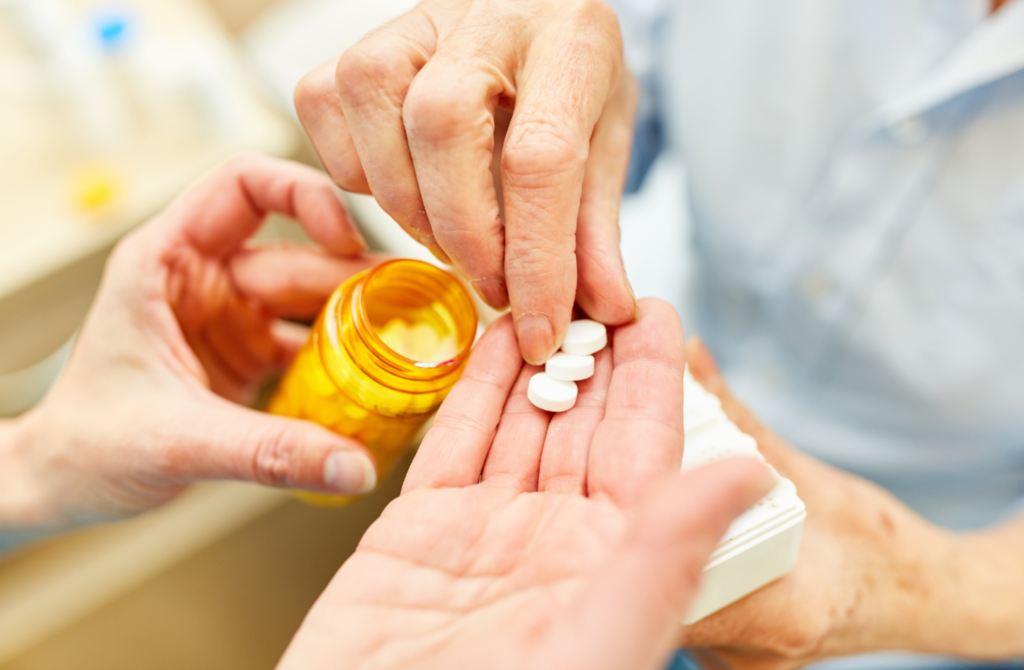 Manos entregando pastillas desde un frasco a un adulto mayor