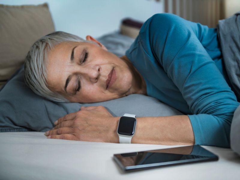 Mujer mayor durmiendo en la cama con un reloj inteligente en la muñeca