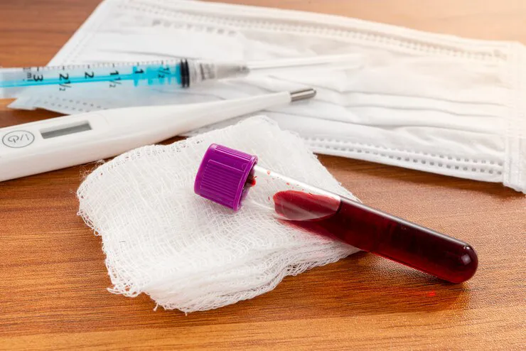 Tubo con muestra de sangre, jeringa, termómetro y mascarilla sobre una mesa