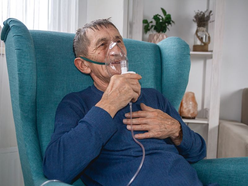 Adulto mayor usa mascarilla de nebulización sentado en un sillón