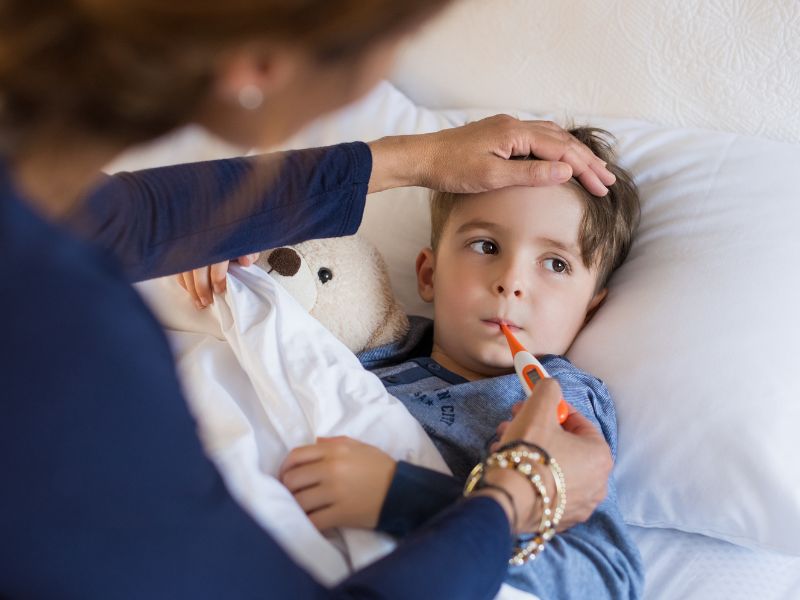 Madre toma la temperatura a un niño enfermo en cama