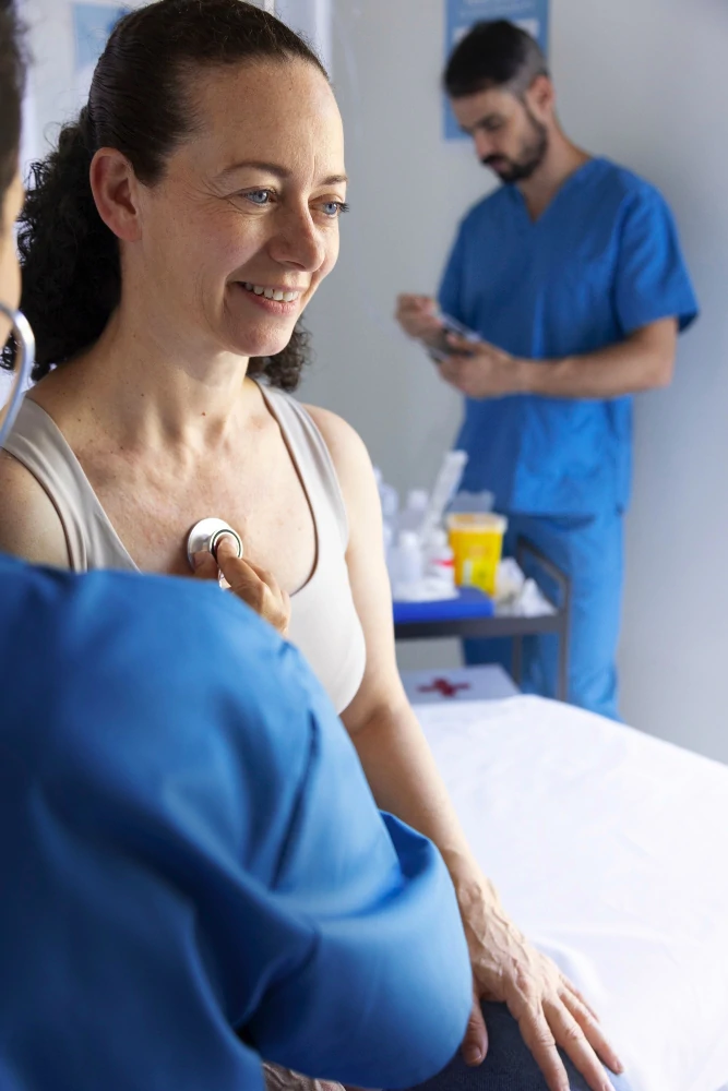 Mujer sonriente es auscultada con estetoscopio por un profesional de salud