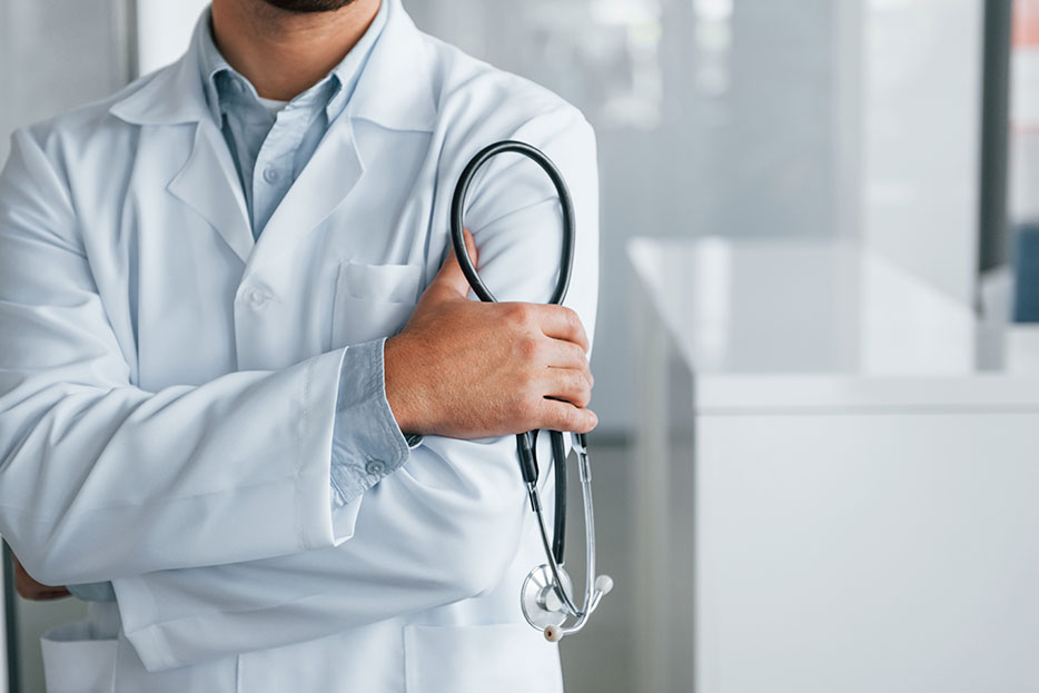 Médico con delantal blanco sostiene un estetoscopio con los brazos cruzados