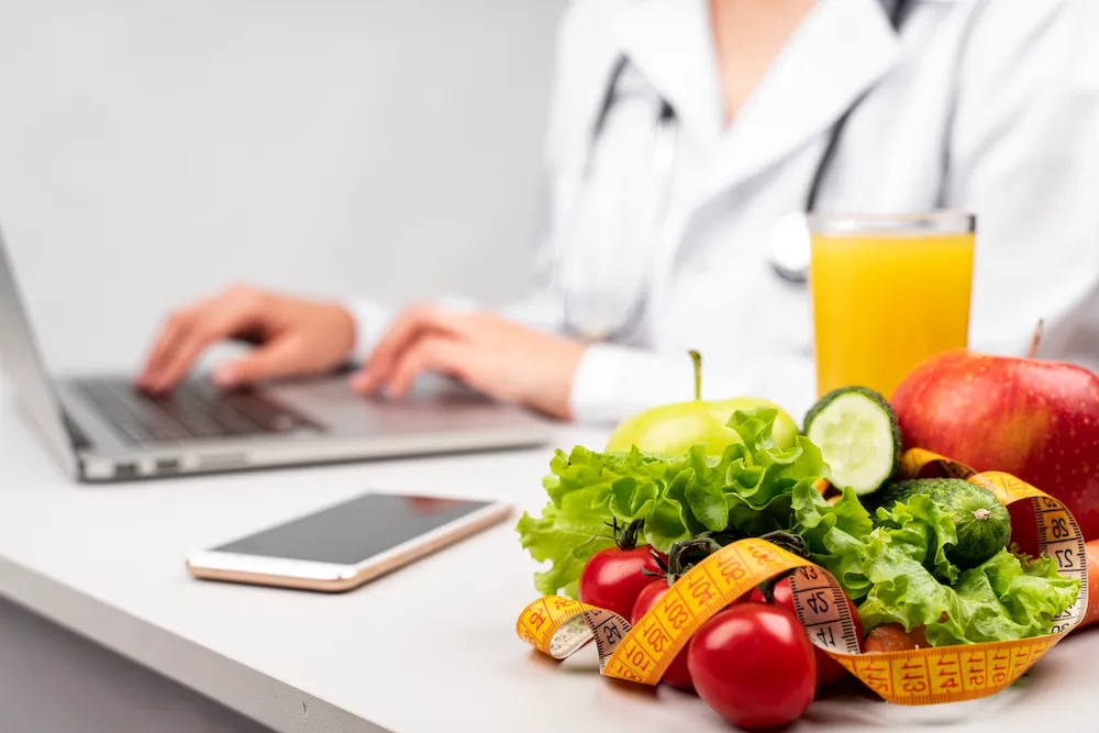 Nutricionista frente a un notebook junto a frutas, verduras y cinta métrica